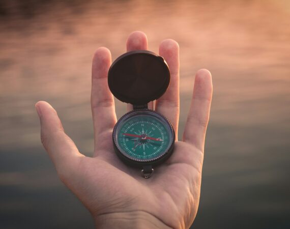 person holding black and green compass pointing to west