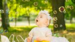 a baby sitting in the grass with bubbles in the air