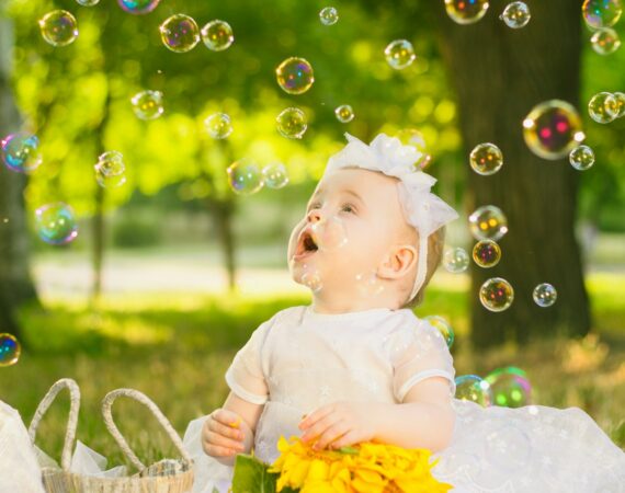 a baby sitting in the grass with bubbles in the air